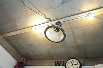 天井パネルを解体して露出させたコンクリートに開けられていた穴を利用して取り付けた照明器具。ベースとなる木材にスライド式の配線レールを取り付けることで照明を好きな位置に移動可
